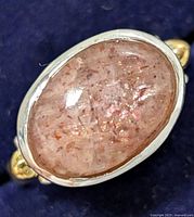 Close-up of oval pink gemstone set in sterling silver ring with gold-tone accents