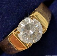 Close-up photo of silver band with round moissanite stone, showing gemstone details and setting.