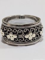 Close-up angle showing detailed floral design with silver flowers on dark oxidized background and inner ring band stamped '925'.