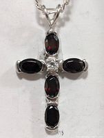 Close-up photo of the silver cross pendant with six garnet stones and one clear center stone.