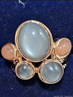 Top view of silver ring showing three translucent grey cat's eye style stones and two coral colored round stones set in gold-toned bezels.