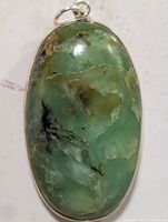 Clear front view of the oval green gemstone pendant set in silver, showing the stone's uneven color patterns and polished surface.