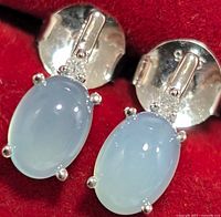 Close-up image showing two silver earrings with oval light blue chalcedony stones held by four prongs each.