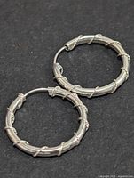 Top-down view of one silver hoop earring showing the bamboo-textured design and clasp mechanism