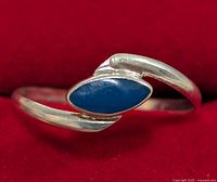Close-up front angle of silver ring showing blue marquise-shaped stone and open band design on red background.