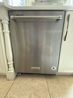 Exterior front view of stainless steel dishwasher installed under counter between white cabinets