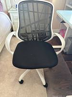 Front view of white desk chair with black mesh backrest and black padded seat cushion, showing armrests and caster wheels.