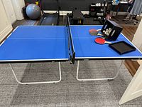 Full view of the unfolded junior sized ping pong table in a room with paddles, net, and balls placed on one end.