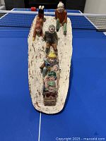 Top-down image showing seven children on a sled and one standing figure, detailed facial expressions and hand-painted features visible.