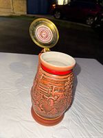 Top view of beer stein interior and hinged lid open showing inside top of lid with firefighting emblem.
