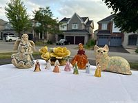 Entire set of 11 porcelain and ceramic figurines on a white surface outdoors, showing the various figures including angel, floral, cat, and lady figurines.
