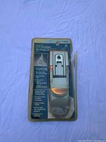 Front of original packaging showing LED booklight through plastic blister. Packaging is damaged but sealed. Includes printed text on front with features.