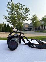 Front angled view of Sony Alpha 200 DSLR with 75-300mm lens and Sony strap displayed outdoors on white surface