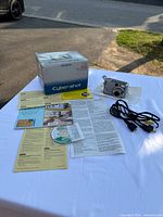 Sony Cyber-shot DSC-S60 digital camera, original box, paperwork, CD with software, and USB cable laid out on white surface in natural outdoor light