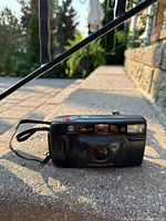 Front view of the Minolta Freedom AF 35R 35mm film camera showing lens, flash, sensor area, and attached black wrist strap.