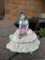 Front angle view of the Royal Doulton Daydreams figurine showing the Victorian lady in pastel dress and bonnet, holding flowers.