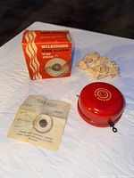 Red Wilkinson fire alarm with original instruction sheet, box, and packaging paper displayed on white surface