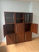 Front view of three brown wood cabinets, doors open showing interior shelves