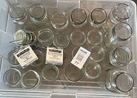 Top view of plastic tote containing assorted clear glass Mason jars in varied sizes with two Bernardin lid boxes and loose lids