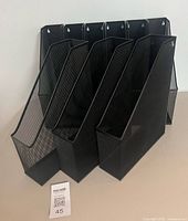 Front view of nine black metal mesh file holders standing together