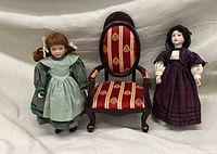 Two porcelain dolls from the Little Women series by Wendy Lawton for Ashton Drake, displayed standing on either side of a small wooden upholstered chair suitable for 18-inch dolls.