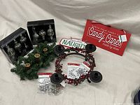 Photo showing Christmas decorations including two wrought iron red berry wreath candle holders, one adorned with faux greenery, two wooden signs labeled "Naughty" and "Very Nice," two boxes of silver hanging ornaments, two packs of silver snowflake craft decorations, and a red "North Pole Candy Canes" sign.