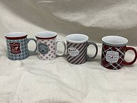 Four Christmas-themed ceramic mugs with festive patterns and holiday text.