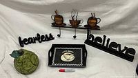 Photo showing wooden signs 'FEARLESS' and 'BELIEVE', metal coffee cup wall hook, large wooden pear, and ceramic coffee tray with coffee cup image. A Sharpie marker is included for scale.