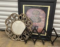 Front view of all three items together: round mirror with ornate gold-tone frame, black framed floral tree art, and expandable peg rack in front of them.