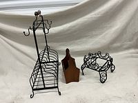 Tall wrought iron cup and plate holder, vintage wooden utensil caddy, and round wrought iron pedestal stand shown together on white backdrop