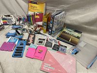 Photo showing a variety of office and school supplies including binders, folders, pens, sticky notes, scissors, magnets, and more laid out on a floor.