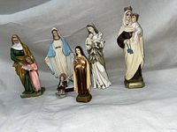 Front view of six vintage plaster religious statues on white fabric background.