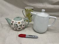 Tea Rex teapot, white coffee pot, tall green leafy mug, red marker for scale