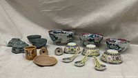 Overview of all items in the lot, showing nested blue bowls, floral nesting bowls, rice bowls with matching spoons, salt and pepper shakers, the small tan plate, and the elephant mug.