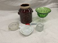 Photo showing all six items on a white cloth background with red and silver Sharpie placed in front for scale, items include a dark brown ceramic crock, a green glass bowl, small textured clear glass container, white ceramic spoon rest, and clear glass ashtray.