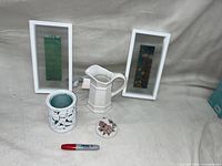 Photo showing two white rectangular frames, white ceramic pitcher, white entwined pattern wax warmer, and a floral beaded coin purse.