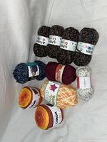 Overview of multiple yarn skeins including Ggh Picasso, Erika Knight, and Caron Cakes yarns in different colors and textures