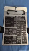 Metal kneeboard front view showing printed checklists and strap