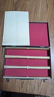 Open metal slide case showing red felt interior, plastic slide rails and paper index sheet
