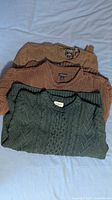 Three folded sweaters stacked: brown Chaps, brown Lands' End, green cable knit