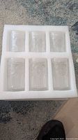 Six pressed glass tumblers in foam tray