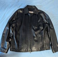 Front view of black leather jacket laid flat, showing collar, zipper, sleeves, and pockets