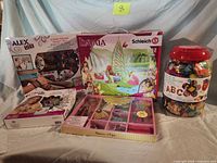 Group shot showing all five items: two Alex DIY bracelet kits, Schleich Bayala playset, foam letter jar, bead craft tray