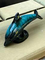 Side view of ceramic dolphin figurine showing green-to-blue drip glaze and wave base.