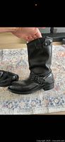 Side view of one black leather engineer boot showing adjustable buckle strap near the ankle and smooth leather finish.