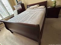 Front angled view of cherry queen sleigh bed showing curved headboard and footboard, mattress on frame, set in bedroom near window.