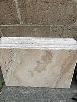 Stack of 5 or more natural stone tiles with beige and tan marbled veining, showing textured edges