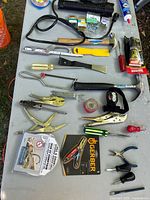 Top-view image showing all tools arranged on a table including hammers, locking pliers, screwdrivers, adhesive tubes, tape, headlamp, and packaging for new items.