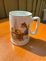 Full view of porcelain mug showing the grandfather and grandson building a model ship at a barrel table, gold trim on rim and base visible.