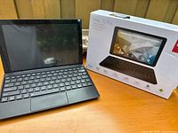 Tablet and detachable keyboard set displayed on a wooden surface alongside original packaging. Device powered off. Keyboard attached and visible in full view.